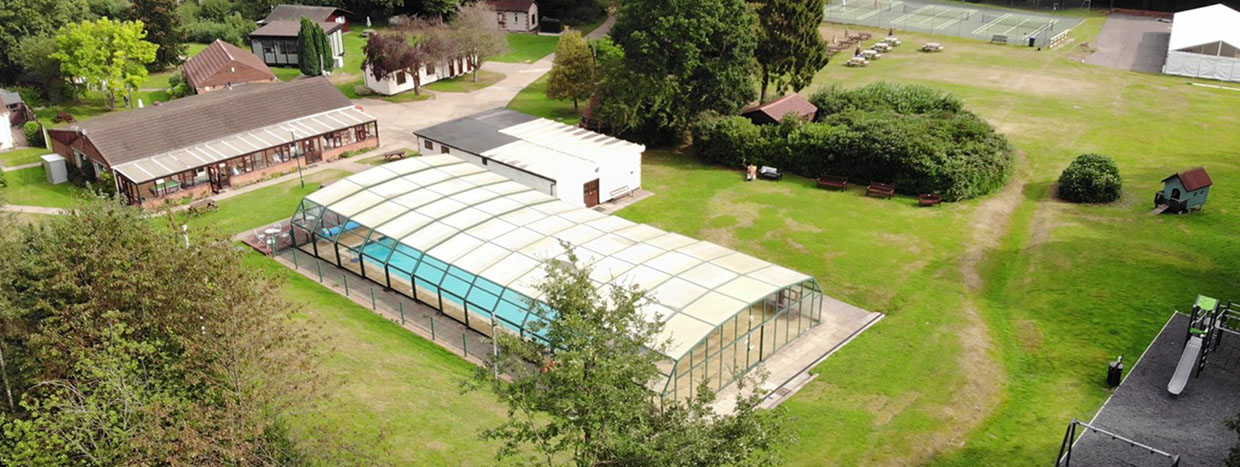 Naturist facilities at Brocken Hurst showing naked swimming pool area and pavilion surrounded by grass and trees and miniten courts for nude sports